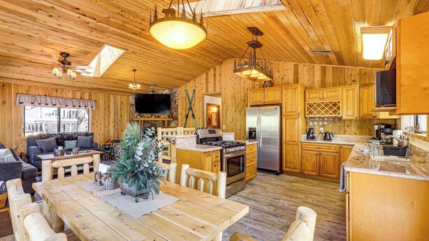 A wooden cabin interior with a dining area, kitchen, and living room. - 2 Mi to Big Bear Lake! Family Haven w/ Hot Tub (Big Bear City)