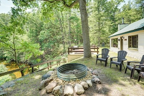 A rustic cabin with a fire pit, outdoor seating, and a view of a forested area.
