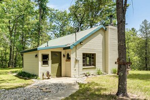A single-story cabin with a green roof, a front door, a small porch, and a welcome sign.