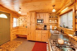 A log cabin interior with wooden walls, a microwave, a sink, and a stove.