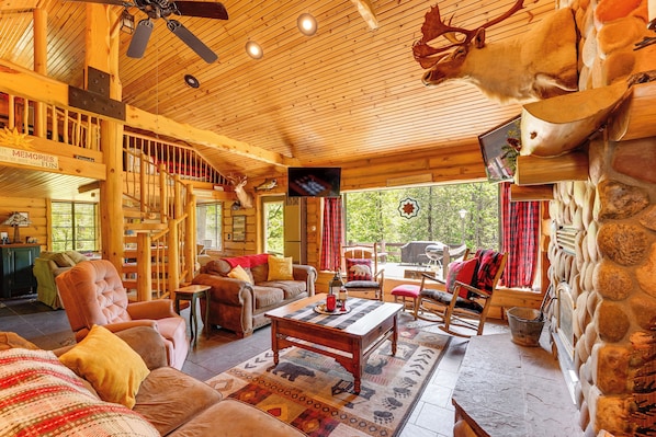 A cozy lodge interior with a wooden ceiling, a fireplace, a television, and a dining area. - Angler Friendly! Pere Marquette Riverfront Retreat (Baldwin)