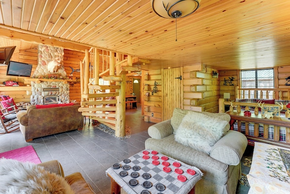 A log cabin interior with a fireplace, wooden furniture, and a checkered table.