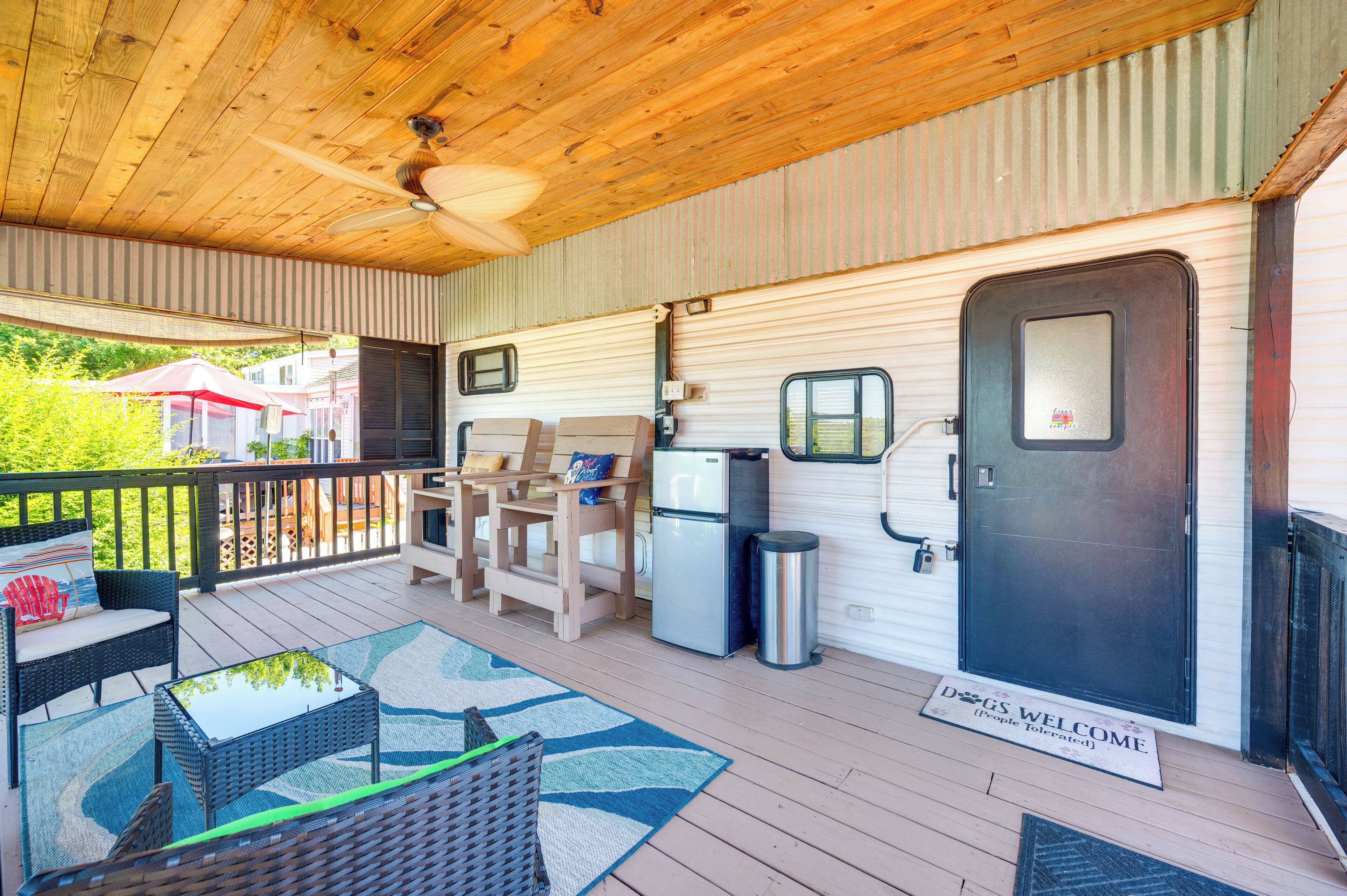 A covered deck with outdoor furniture, a refrigerator, and a door with a welcome mat.