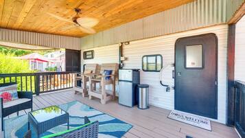 A covered deck with outdoor furniture, a refrigerator, and a door with a welcome mat.