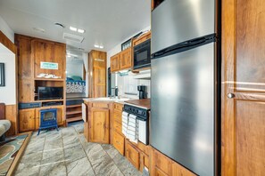 Cocina compacta para autocaravana con armarios de madera, refrigerador de acero inoxidable, microondas y estufa.