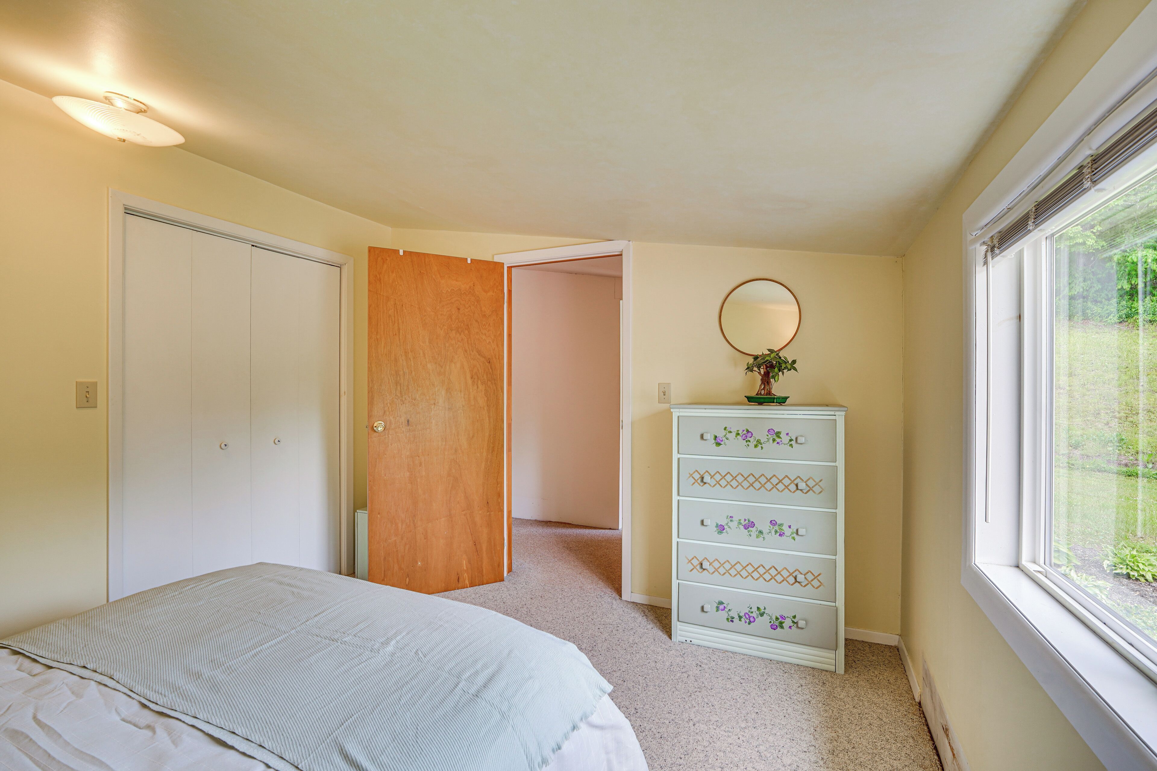 A bedroom with a bed, a dresser, a mirror, and a window.
