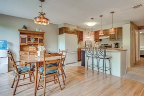 Une cuisine avec des meubles de rangement en bois, un réfrigérateur, une table à manger avec des chaises et des luminaires suspendus.