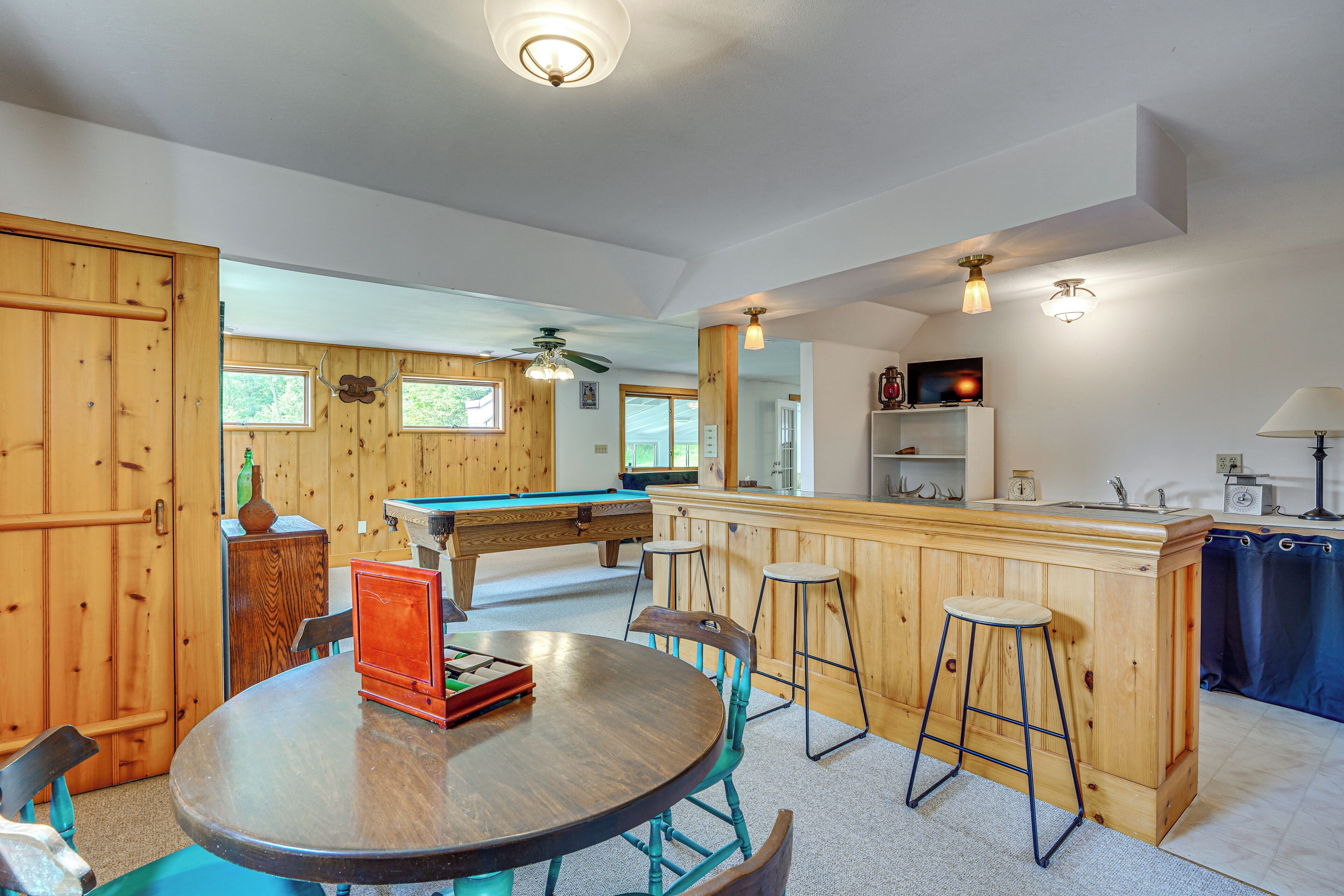 A pool table, bar area, and wooden walls in a room with a ceiling fan.