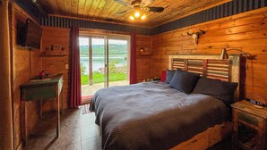 Ein Schlafzimmer einer Holzhütte mit Bett, Schreibtisch, Stuhl, Deckenventilator und Blick ins Freie.