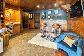 A rustic interior with wooden walls, a bar area with stools, and a blue sofa.