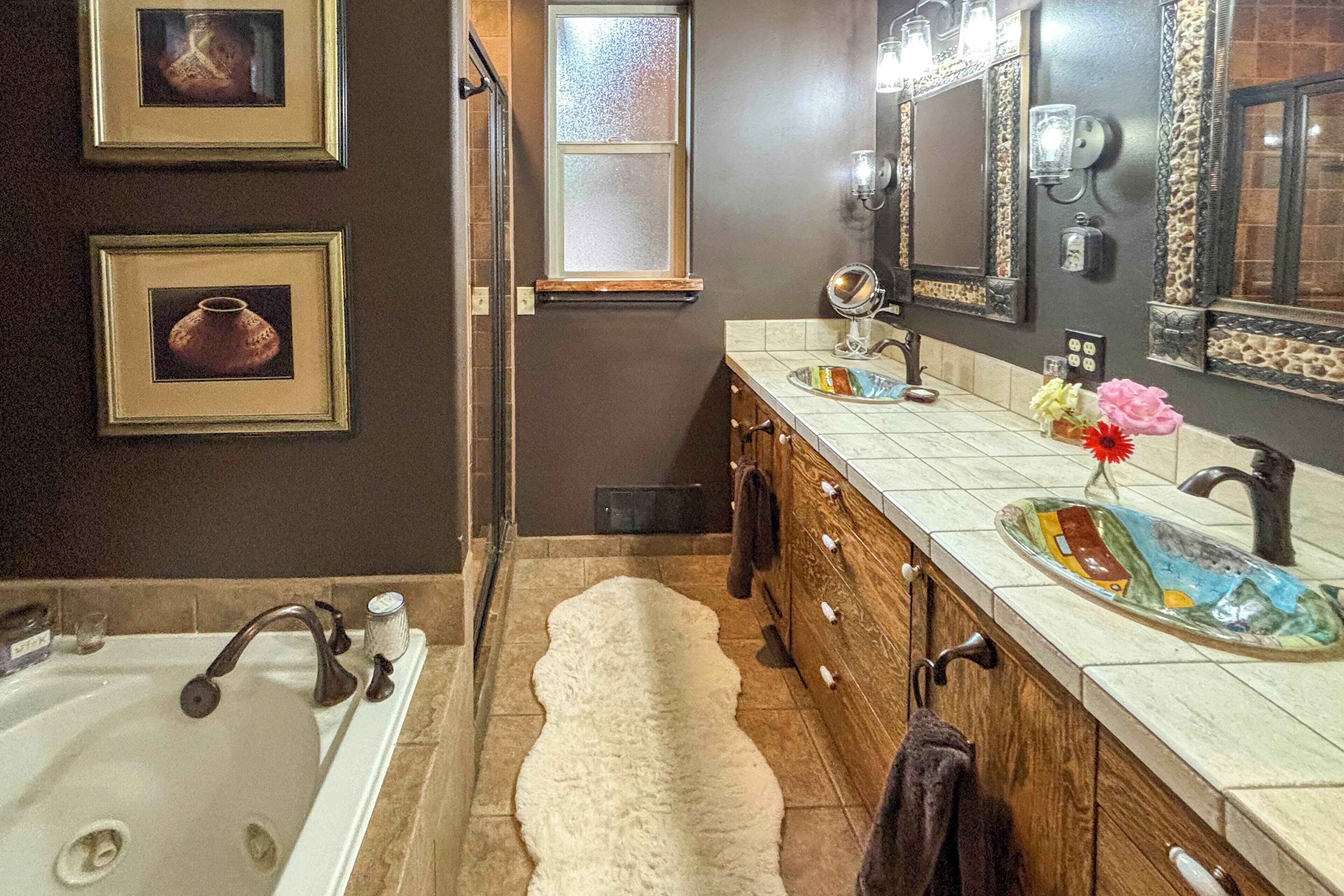 A bathroom with a bathtub, a vanity with a mirror, a sink, and framed pictures on the wall.