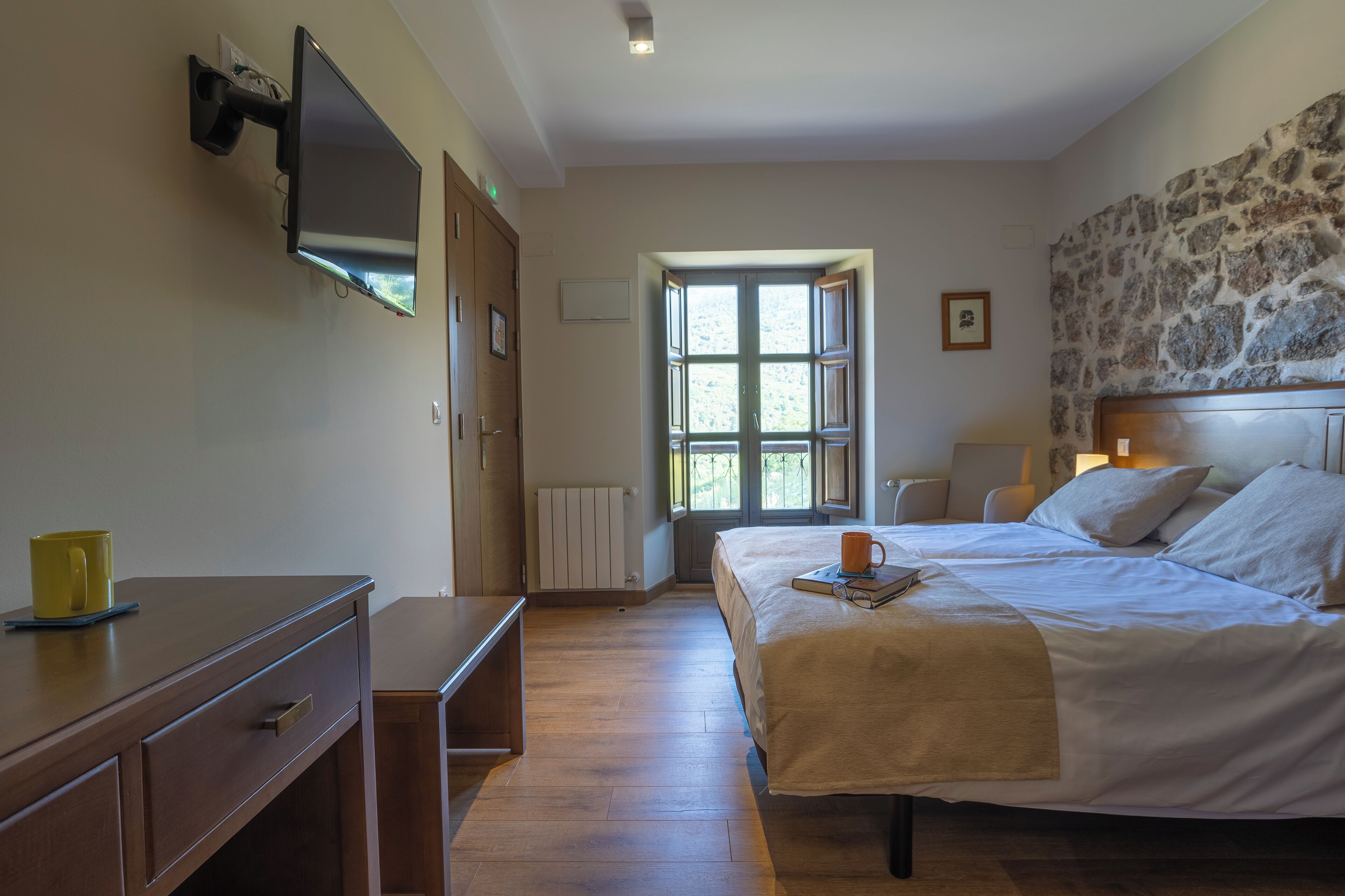A bedroom with a bed, bedside table, and a TV mounted on the wall.