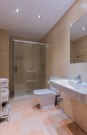 Ein modernes Badezimmer mit einer Duschkabine aus Glas, einer weißen Toilette, einem Waschbecken inklusive Spiegel und einem gefliesten Boden.