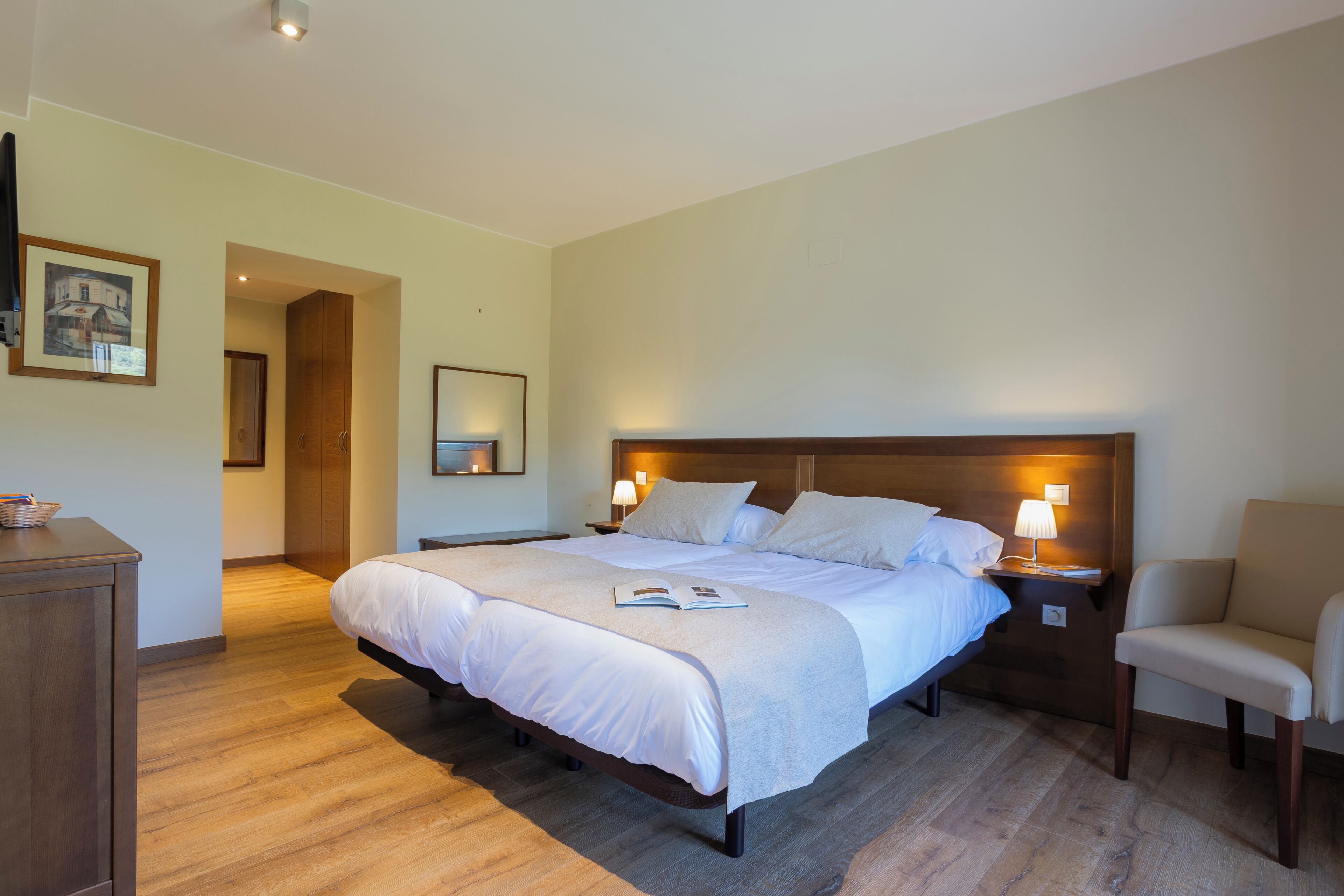 Ein Hotelzimmer mit einem großen Bett, Nachttischen, einem Sessel, einem Holzschrank und einem gerahmten Bild an der Wand.