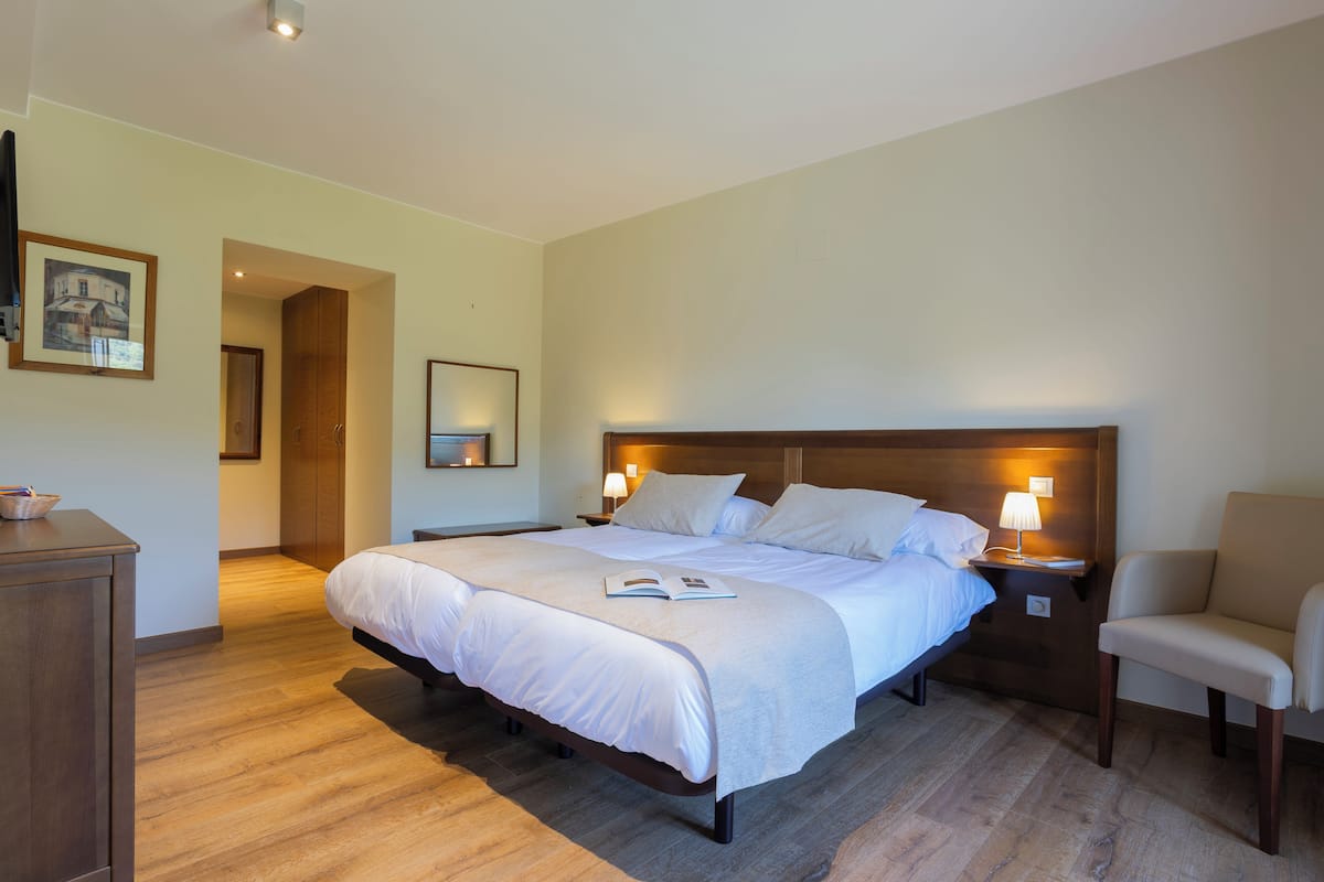 A hotel room with a large bed, bedside tables, a chair, a wooden wardrobe, and a framed picture on the wall.