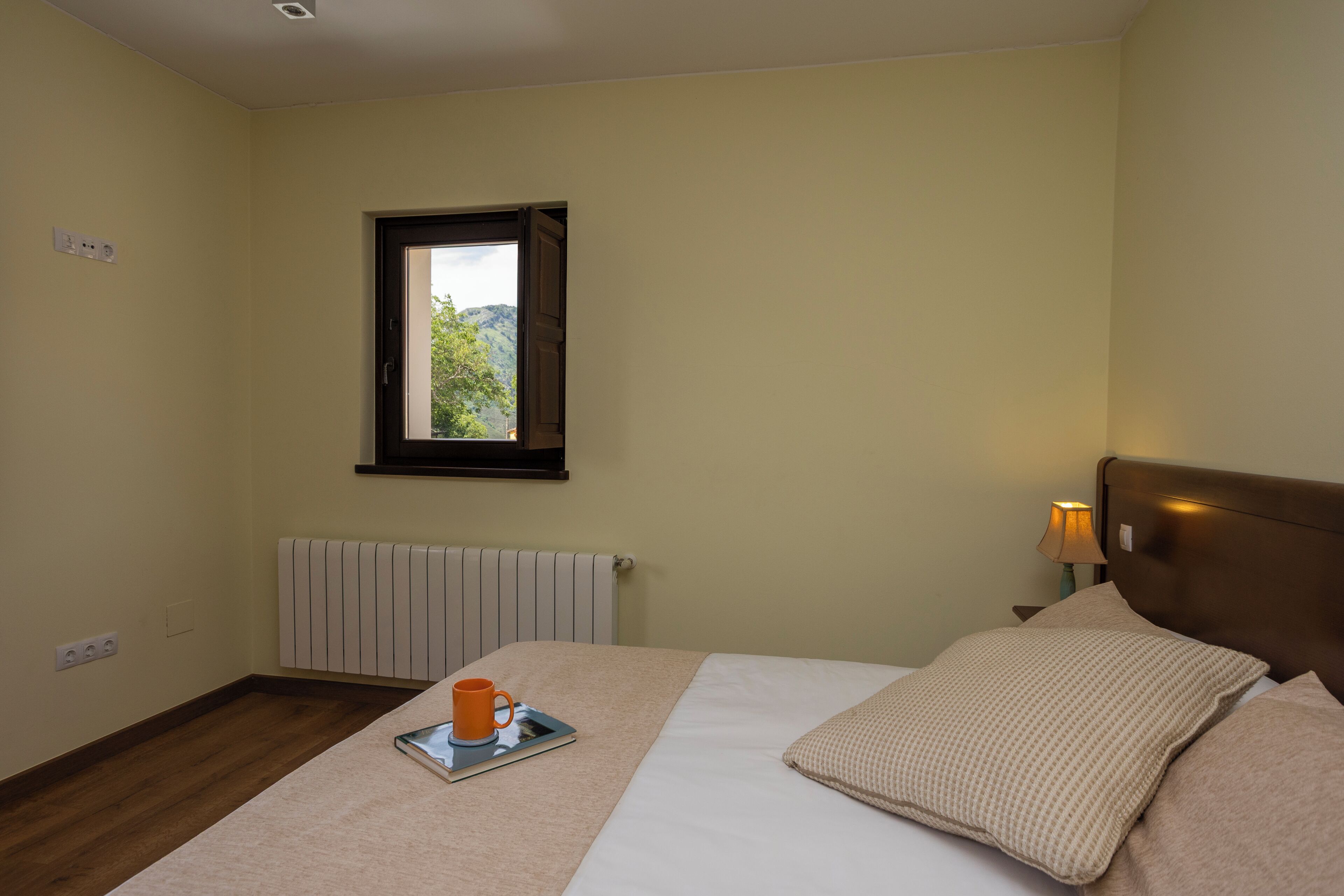 Un dormitorio con cama, ventana con vistas, lámpara de noche y radiador.