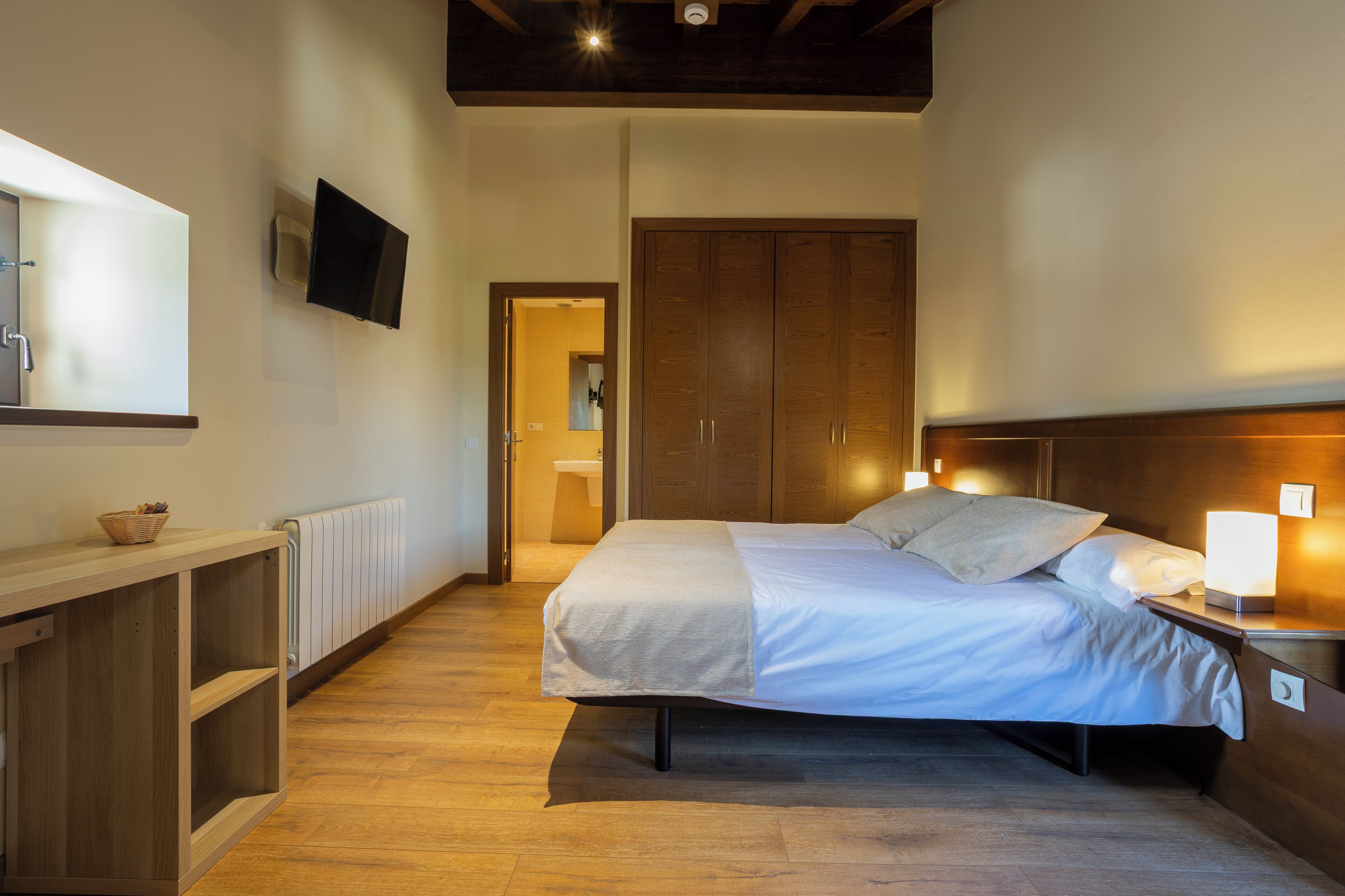 Un dormitorio con cama, mesita de noche, armario de madera y televisor montado en la pared.