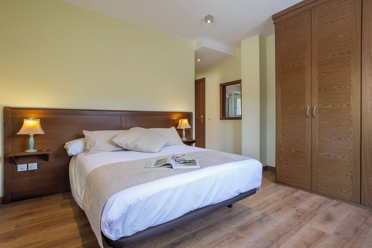 A bedroom with a bed, nightstands, a wooden wardrobe, and a mirror.