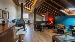 Una habitación amplia con techo alto, vigas de madera, chimenea, zona de comedor y área de estar con sofá y sillones.