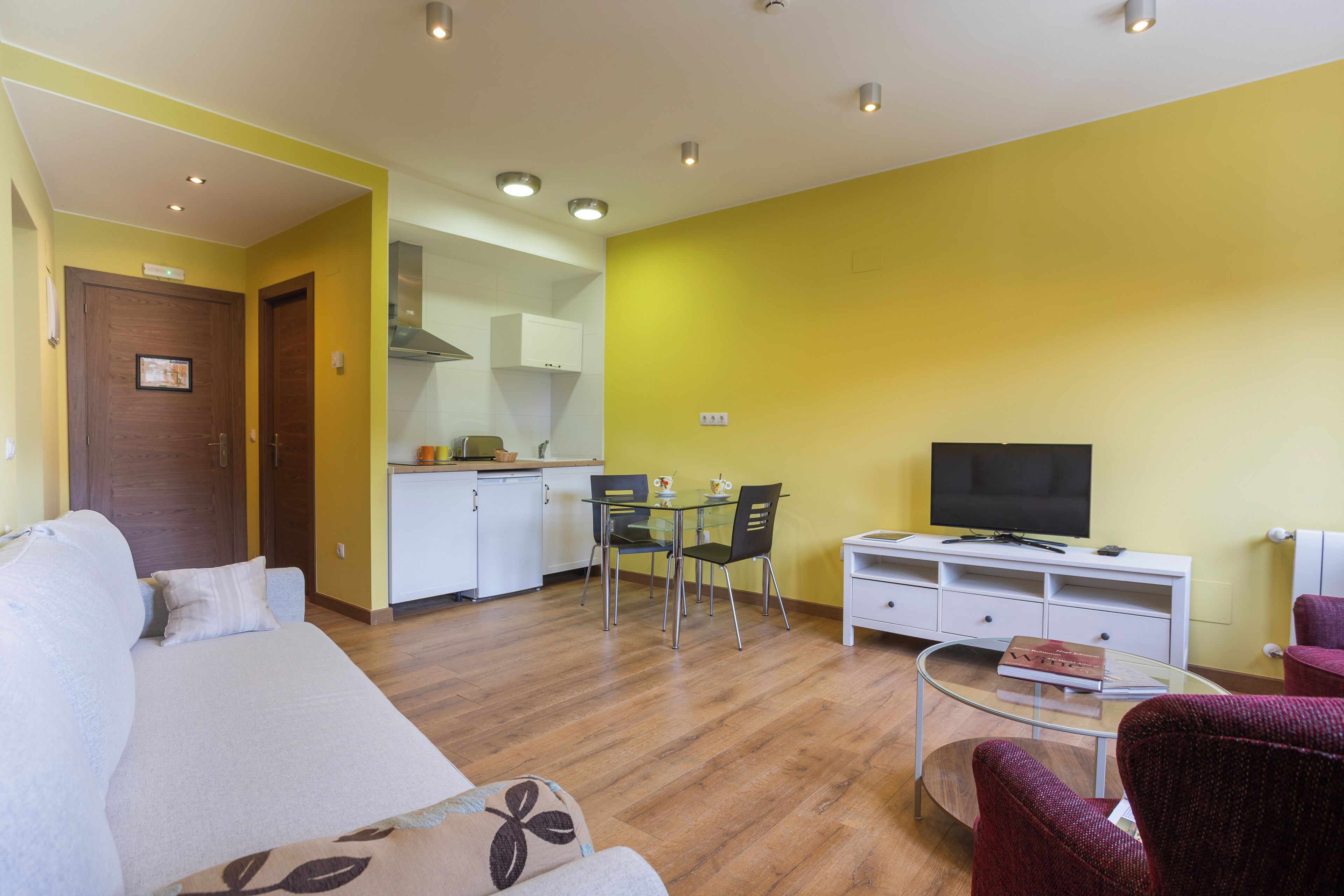 Una sala de estar con un sofá, una mesa de centro de vidrio, un televisor y un comedor con sillas y una mesa.