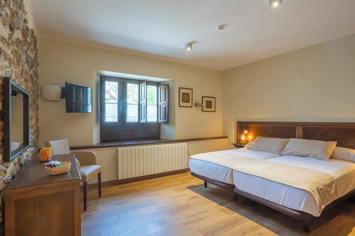 A bedroom with a large bed, a desk with a chair, a window, and a radiator.