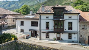 Un edificio de dos pisos con techo de tejas, ventanas grandes y un balcón con macetas.