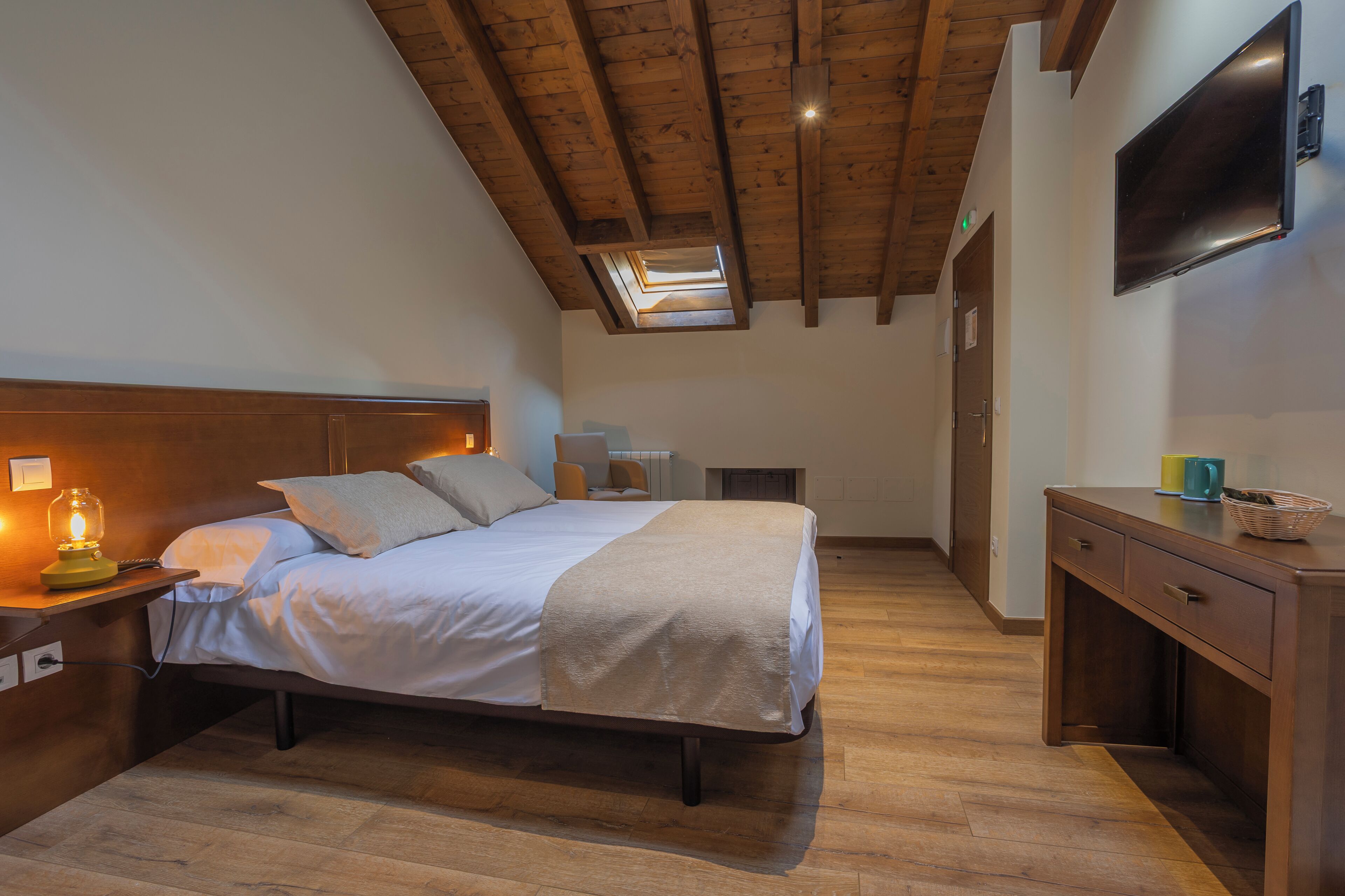 Een slaapkamer met een bed, bedlamp, houten bureau en een aan de muur bevestigde televisie.