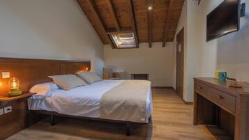 Een slaapkamer met een bed, bedlamp, houten bureau en een aan de muur bevestigde televisie.