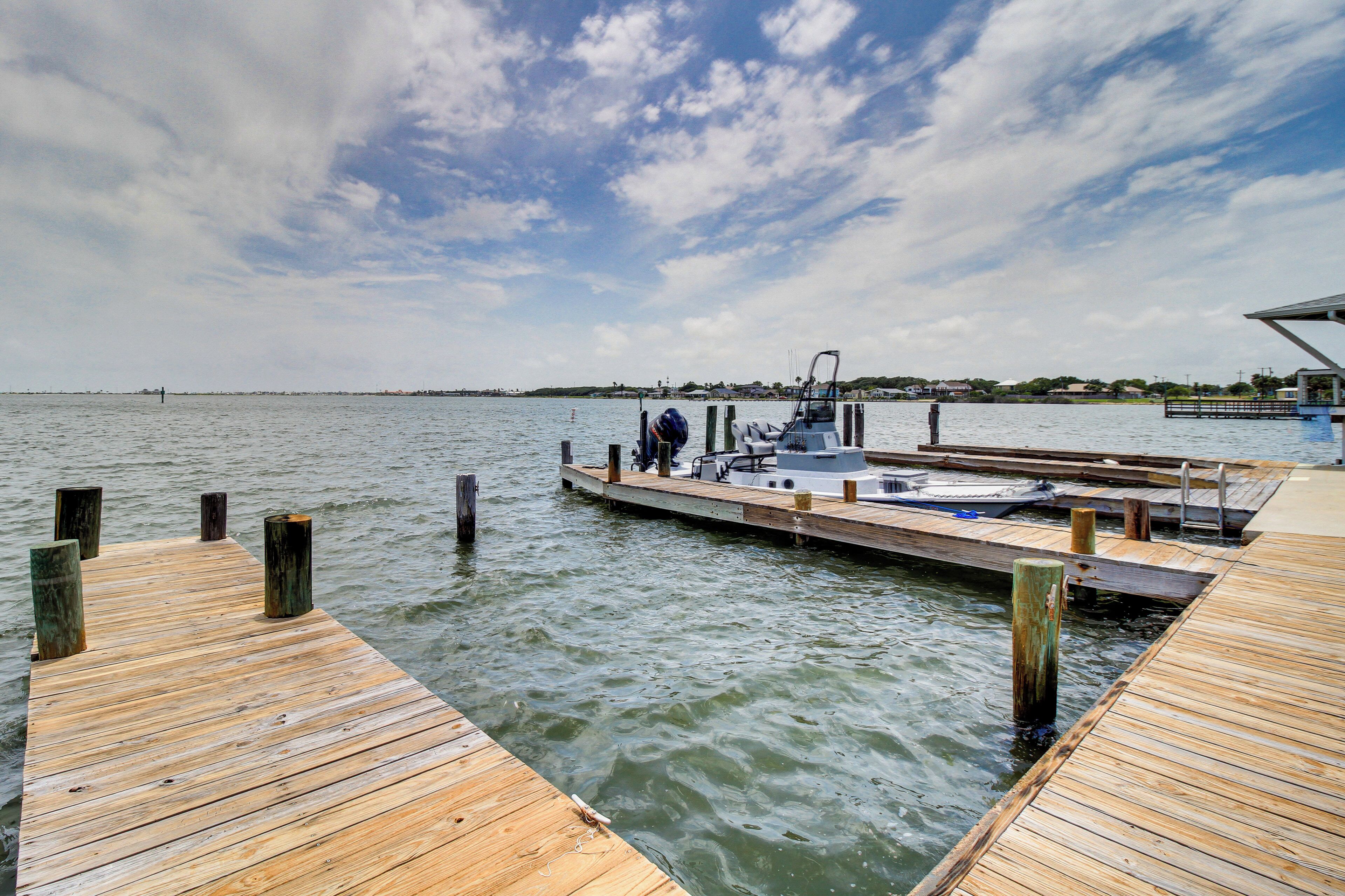 A wooden pier extending into calm water with a docked boat and a distant shoreline.