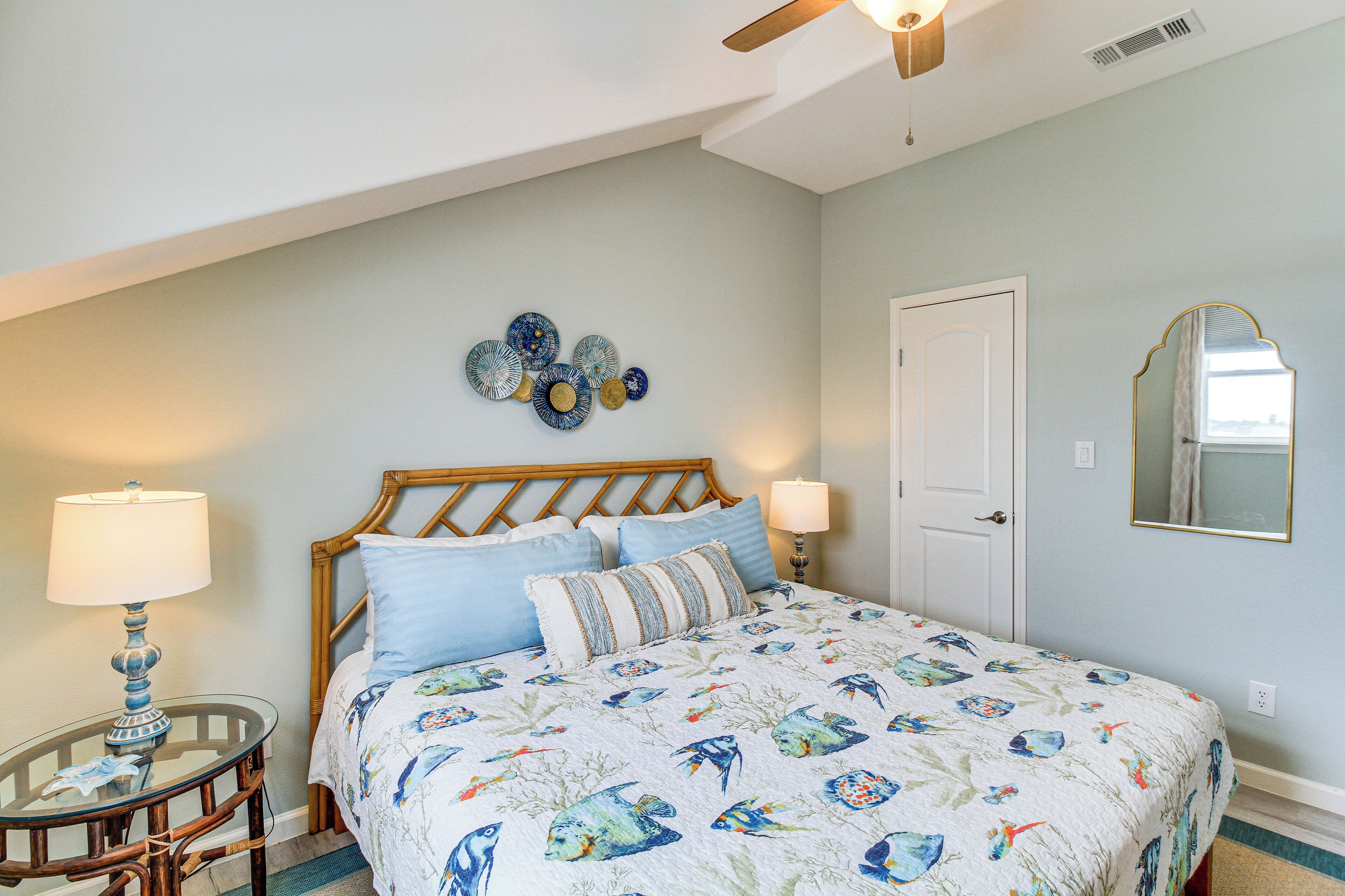 A bedroom with a bed, two bedside tables, a wall clock, a mirror, and a ceiling fan.