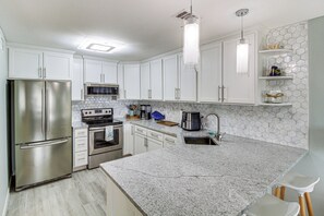 A modern kitchen with white cabinets, stainless steel appliances, a granite countertop, and a hexagonal tile backsplash. - 3BR Condo on the Bay w/ Pool and Perks (Rockport)