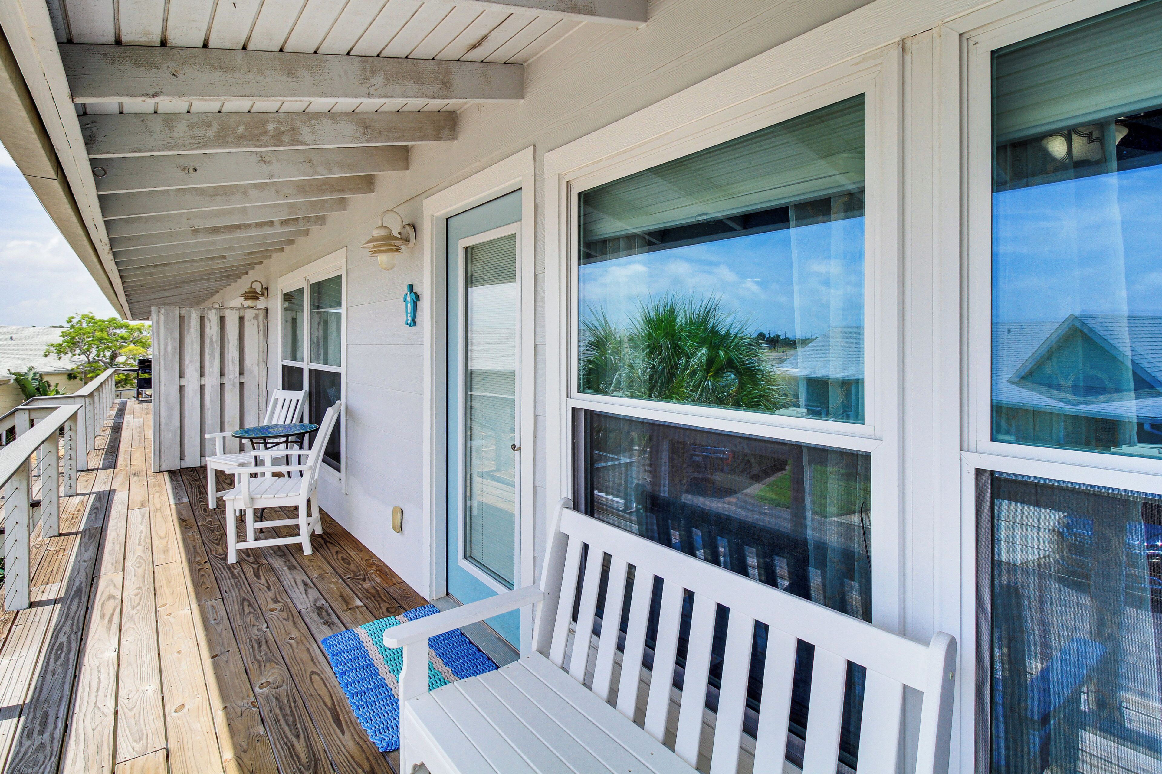 A covered porch with a wooden deck, white railings, and a bench.