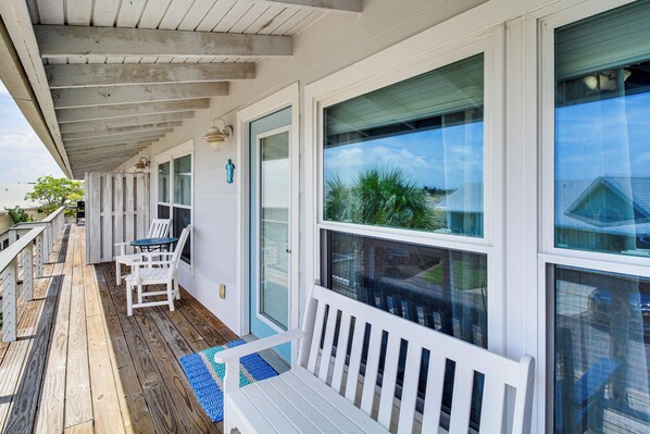 A covered porch with a wooden deck, white railings, and a bench. - 3BR Condo on the Bay w/ Pool and Perks (Rockport)
