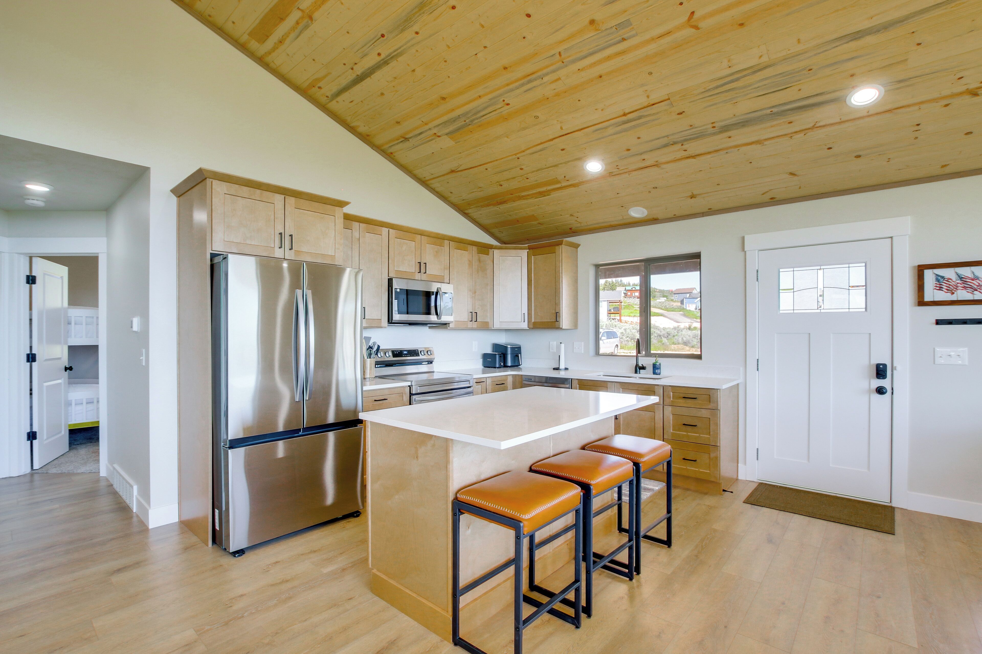 A modern kitchen with wooden ceiling, stainless steel appliances, and a large island with bar stools.