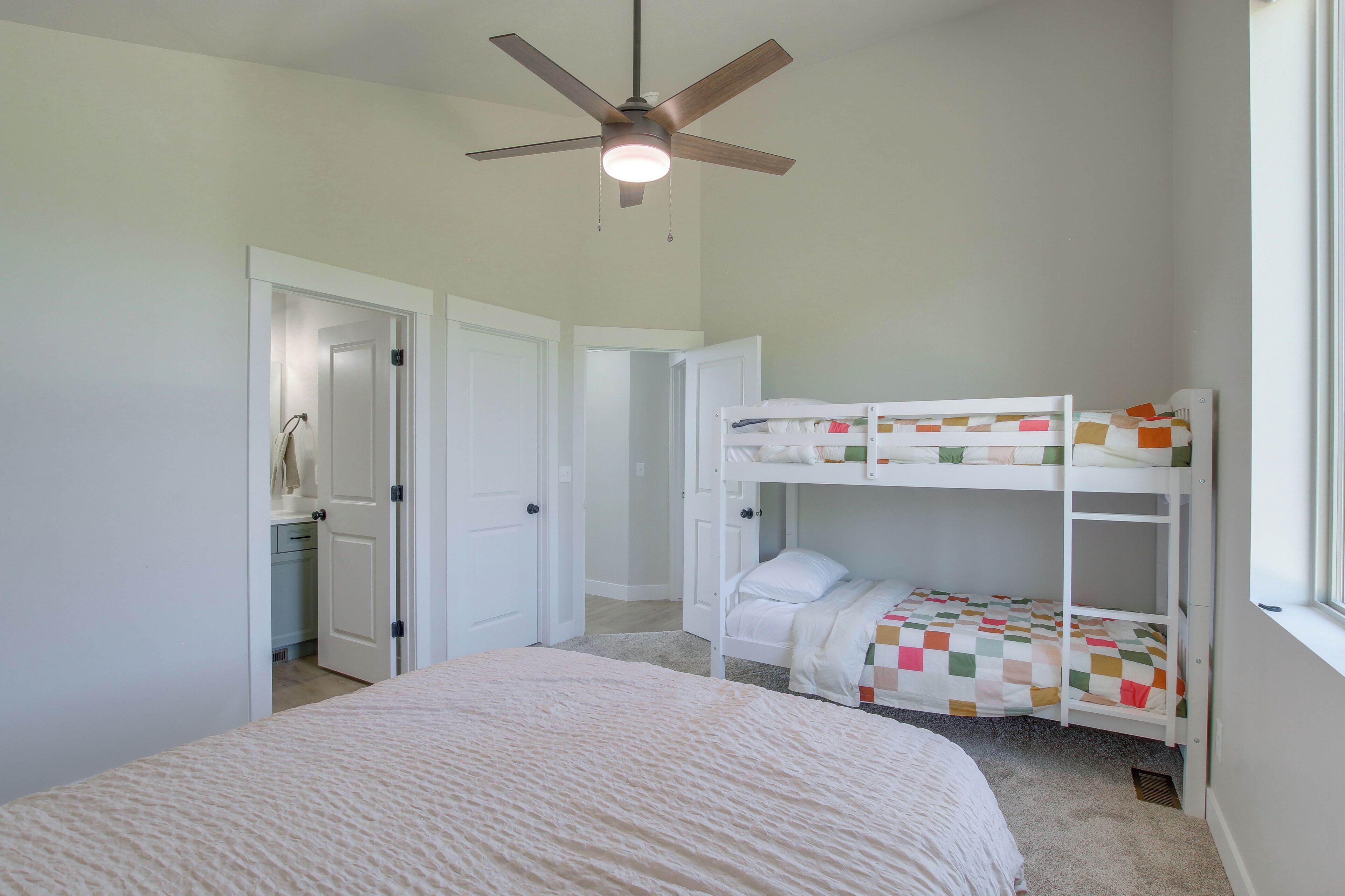 A bedroom with a bunk bed, a ceiling fan, and a door leading to a bathroom.
