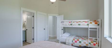 A bedroom with a bunk bed, a ceiling fan, and a door leading to a bathroom.