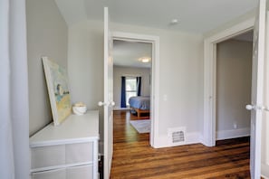 Um corredor leva a um quarto com uma cama, uma mesa de cabeceira e um quadro na parede.