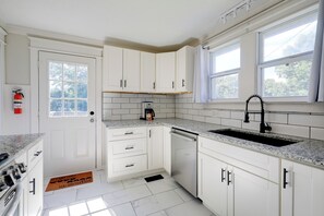 Una cocina con armarios blancos, encimera de granito, lavavajillas y ventana con vista a árboles.