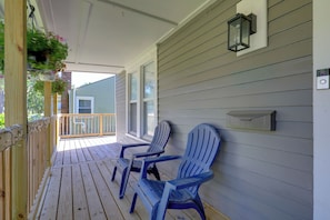 Une véranda en bois avec deux fauteuils Adirondack, une boîte aux lettres et un panier à fleurs suspendu.