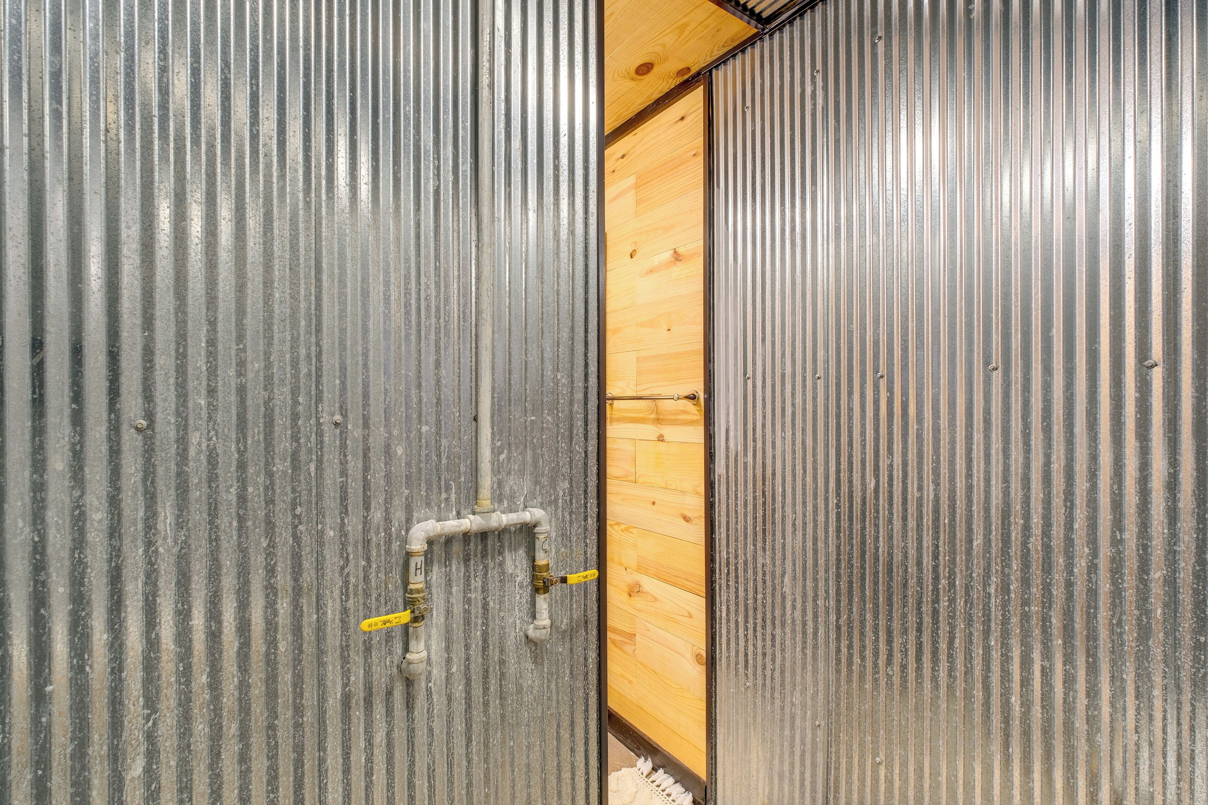 Pared de metal corrugado con un marco de puerta de madera y un accesorio de fontanería visible.