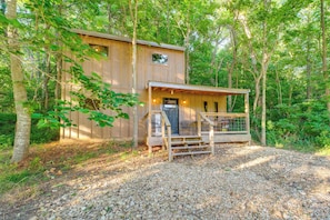 Une cabane en bois avec un porche, entourée d’arbres.