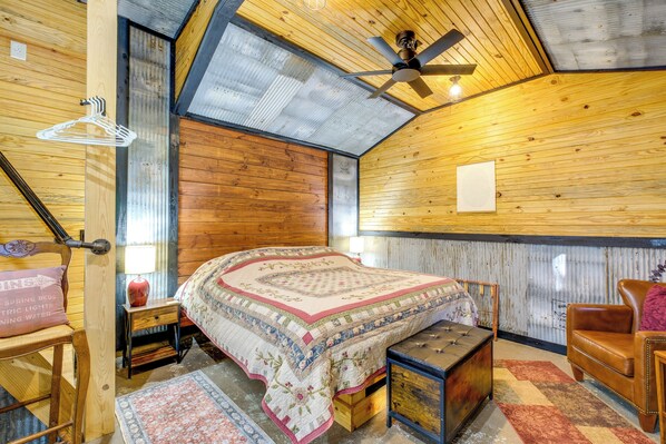 A bedroom with a wooden ceiling, a bed with a quilt, a nightstand, a chair, a hanging light, and a ceiling fan. - Creek Access & On-site Trails: Serene Ozark Cabin (Stella)