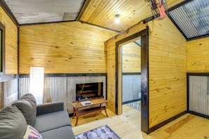 A cozy cabin interior with a wooden interior, a sofa, a small table, and a television. - Creek Access & On-site Trails: Serene Ozark Cabin (Stella)