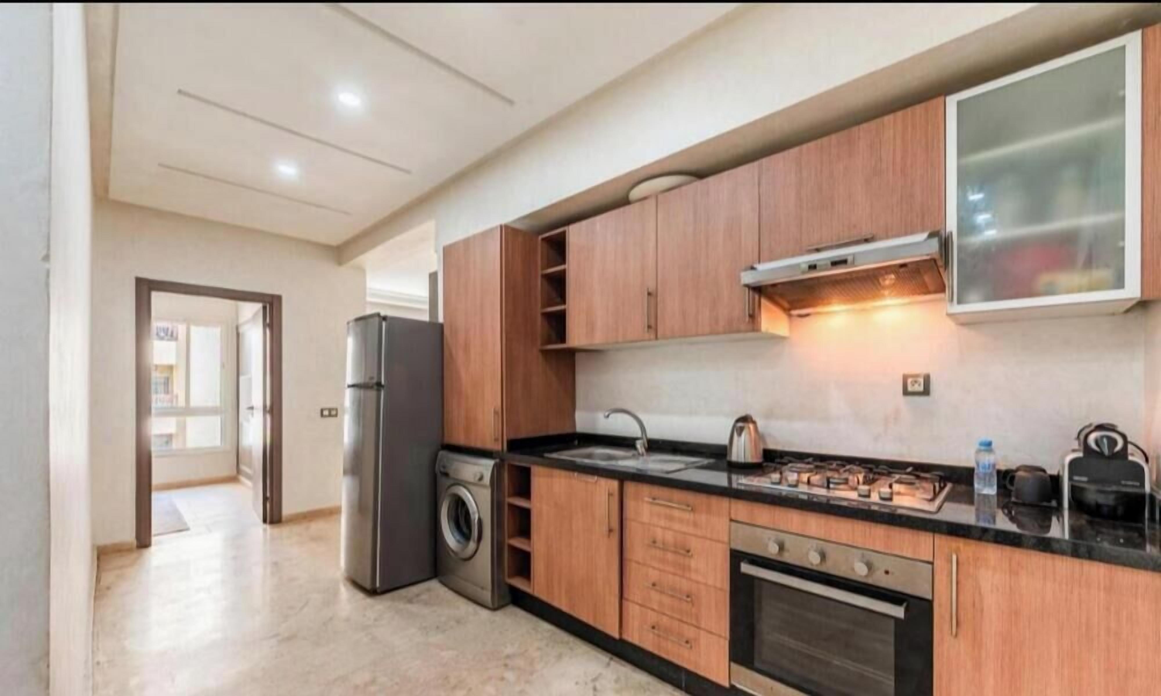 Une cuisine moderne avec des meubles en bois, un réfrigérateur en acier inoxydable, un lave-linge et une cuisinière à gaz.
