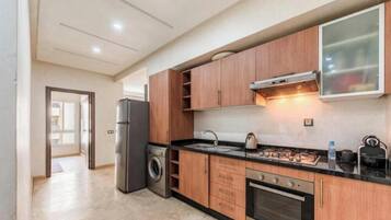 Une cuisine moderne avec des meubles en bois, un réfrigérateur en acier inoxydable, un lave-linge et une cuisinière à gaz.