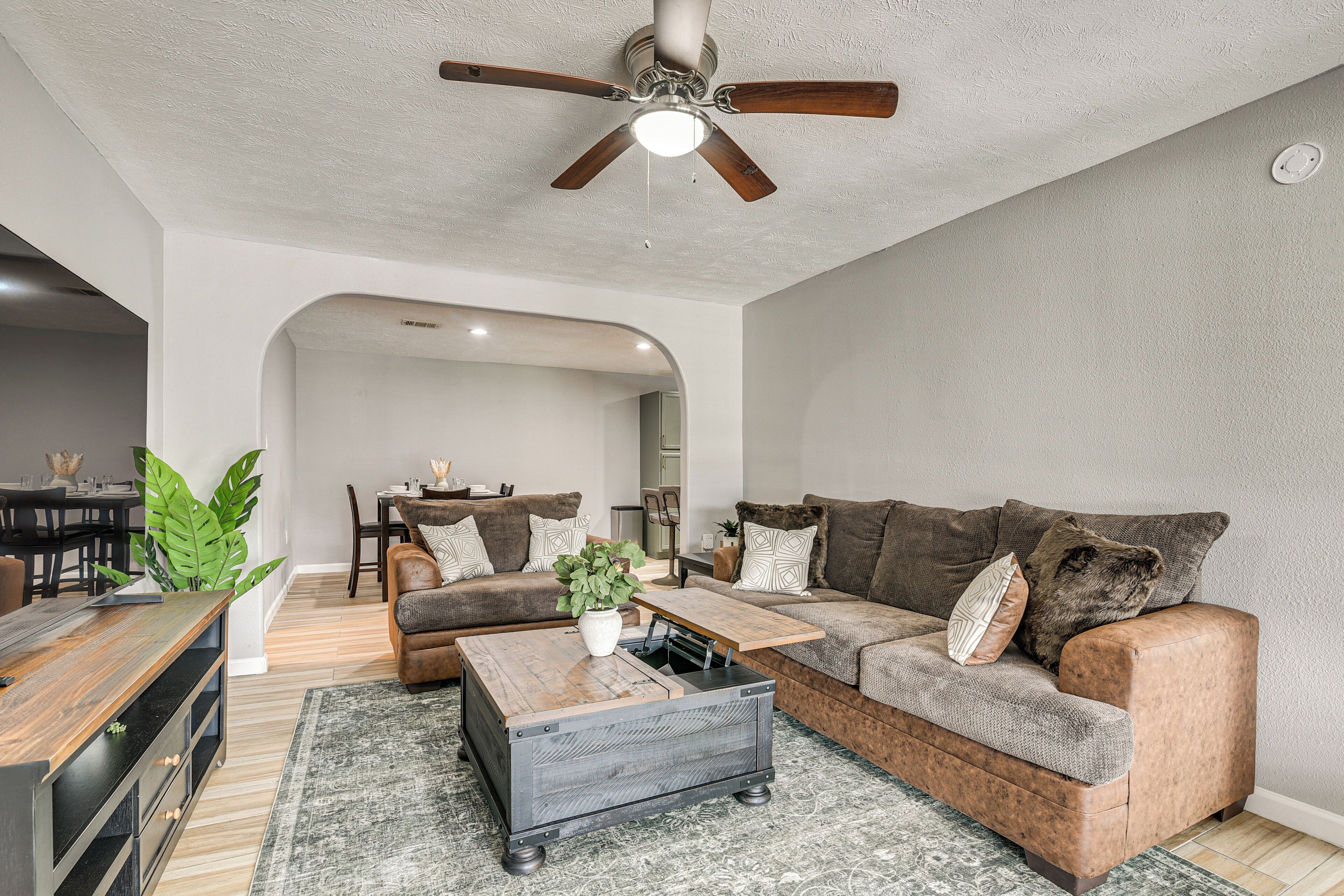 Un salon avec un ventilateur de plafond, un canapé, une table basse et, au fond, un coin repas.