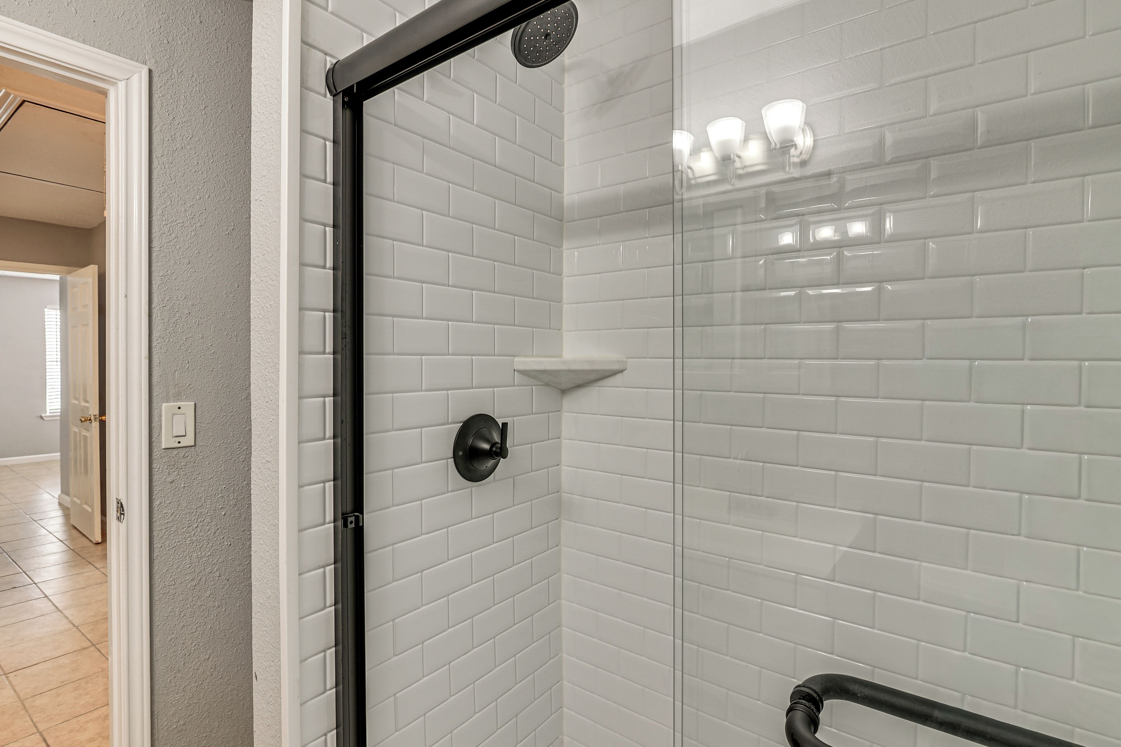 A bathroom with white subway tiles, a glass shower enclosure, a black showerhead, and a white towel rack.