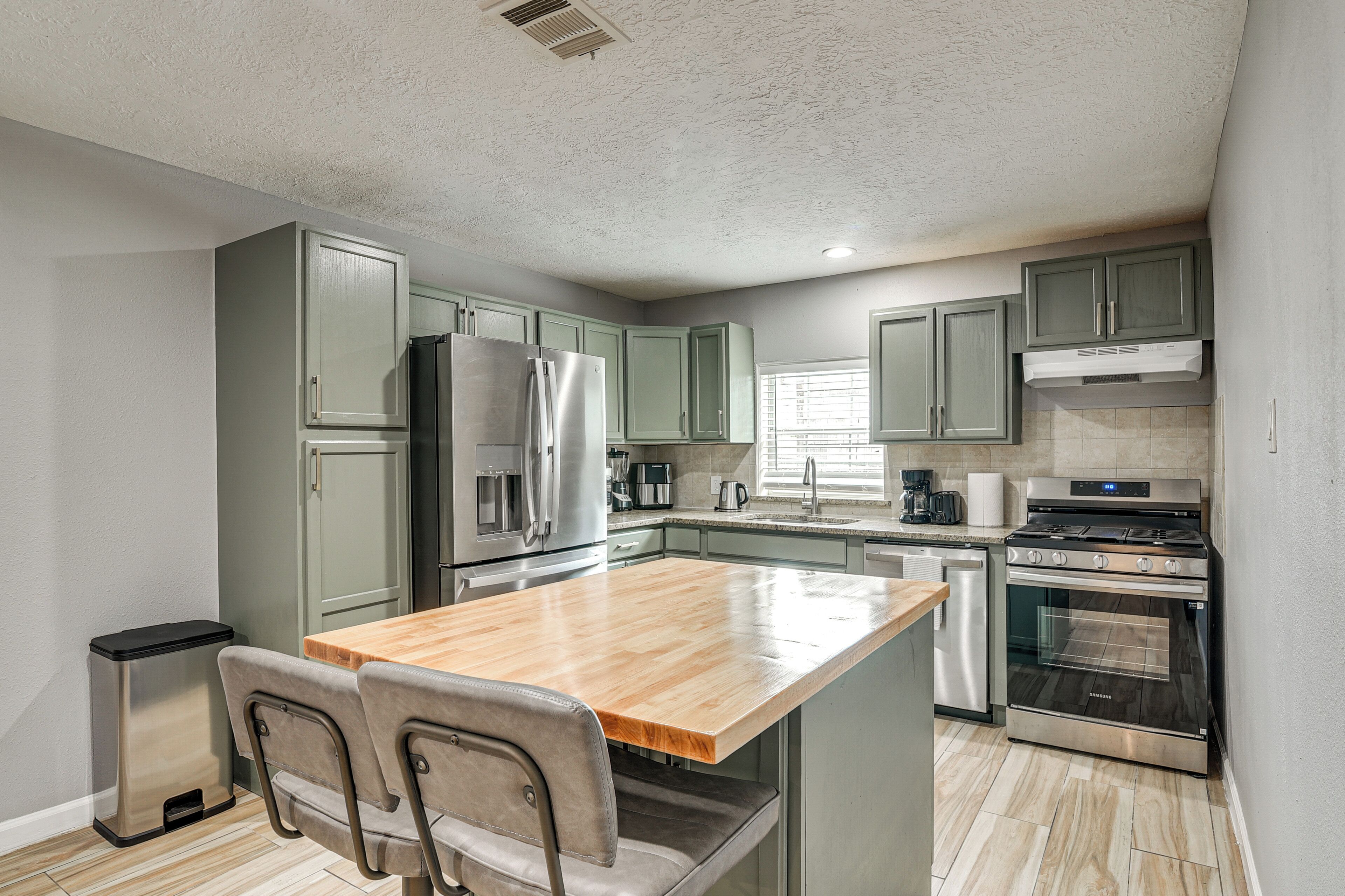 A modern kitchen with a wooden island, stainless steel appliances, and light green cabinets.
