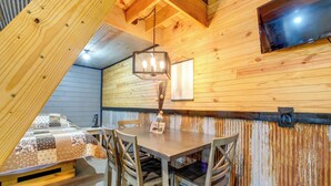 A cozy room with a wooden ceiling, a dining table with chairs, a TV mounted on the wall, and a view of the outside.