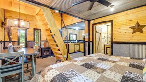 A cozy room with a wooden interior, a quilted bed, a dining table, and a staircase.